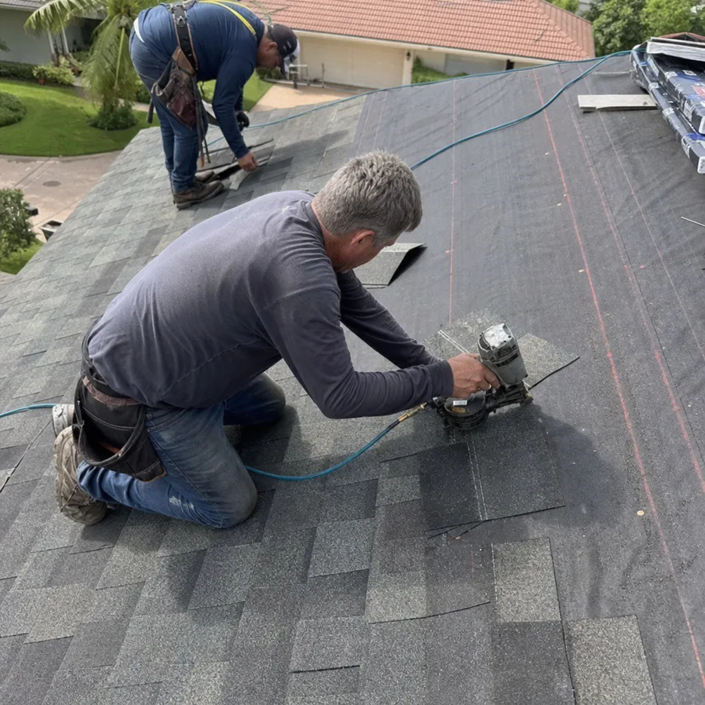 Two professional roofers installing asphalt shingles on a residential roof